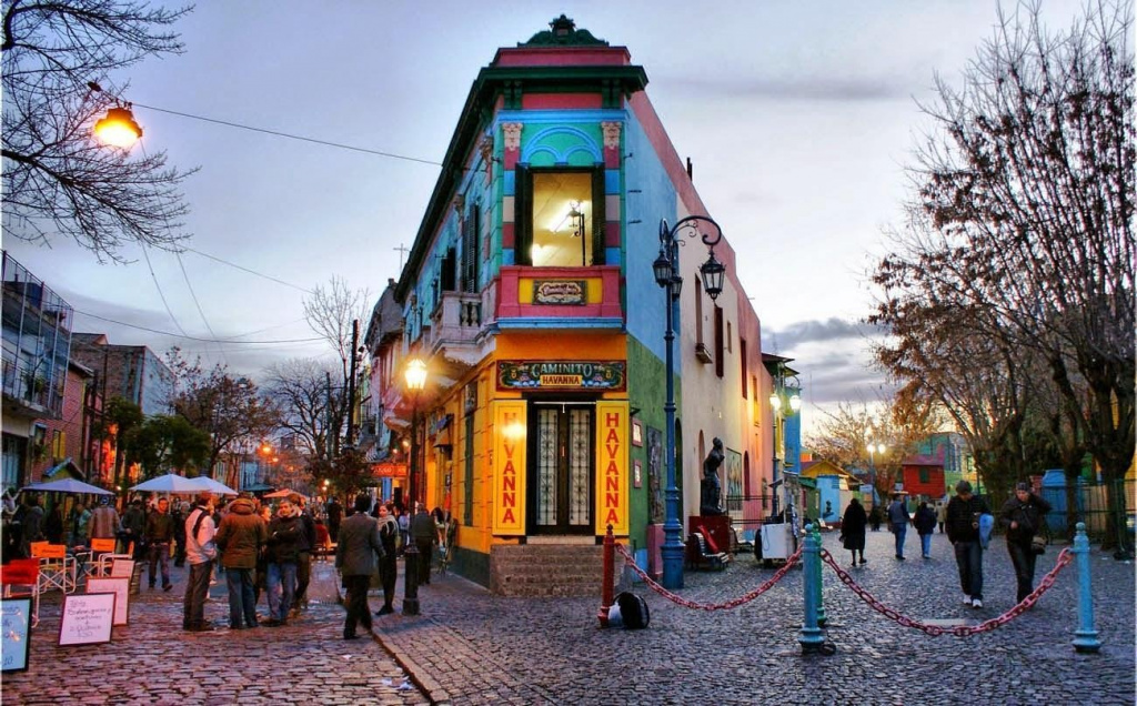 A colorful building on a cobblestone street with La Boca in the background Description automatically generated